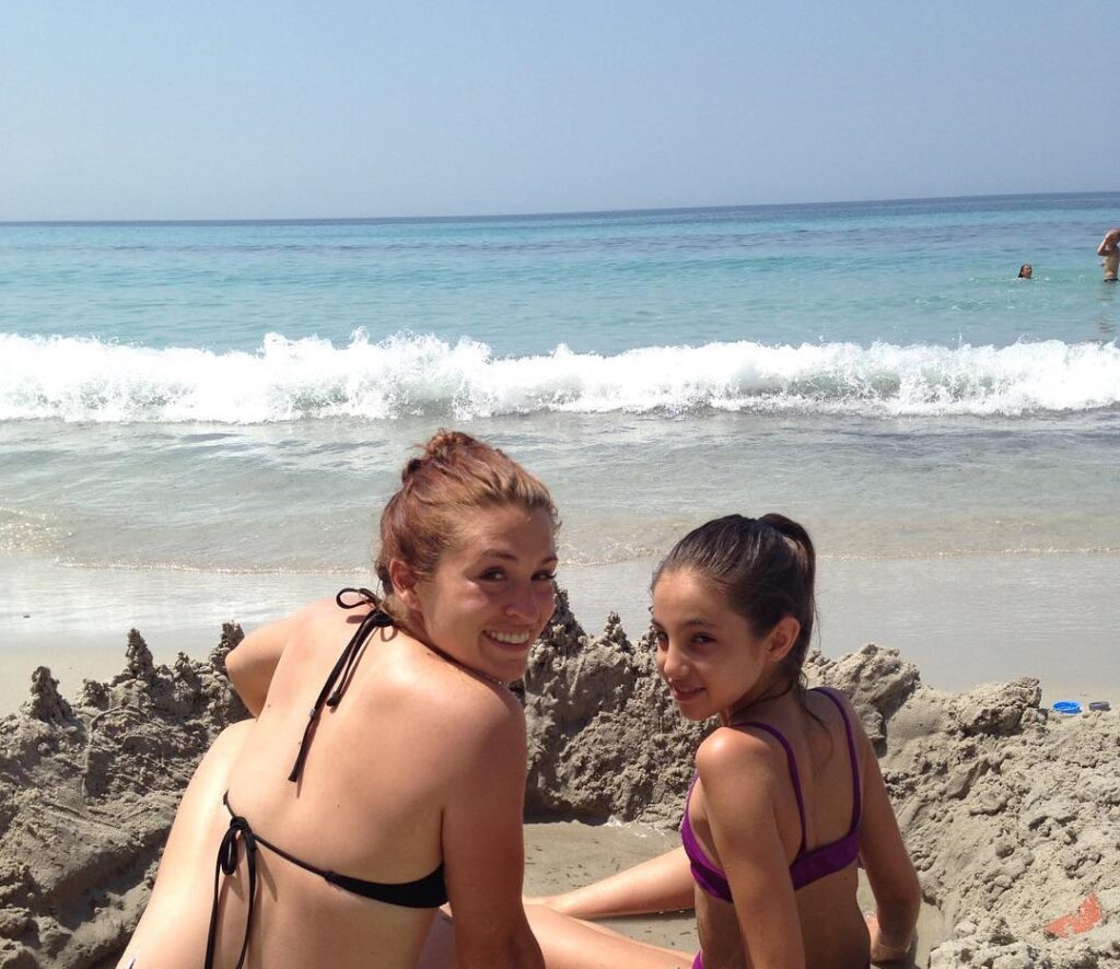 Two young women building sandcastles at a Mediterranean beach on a sunny day.