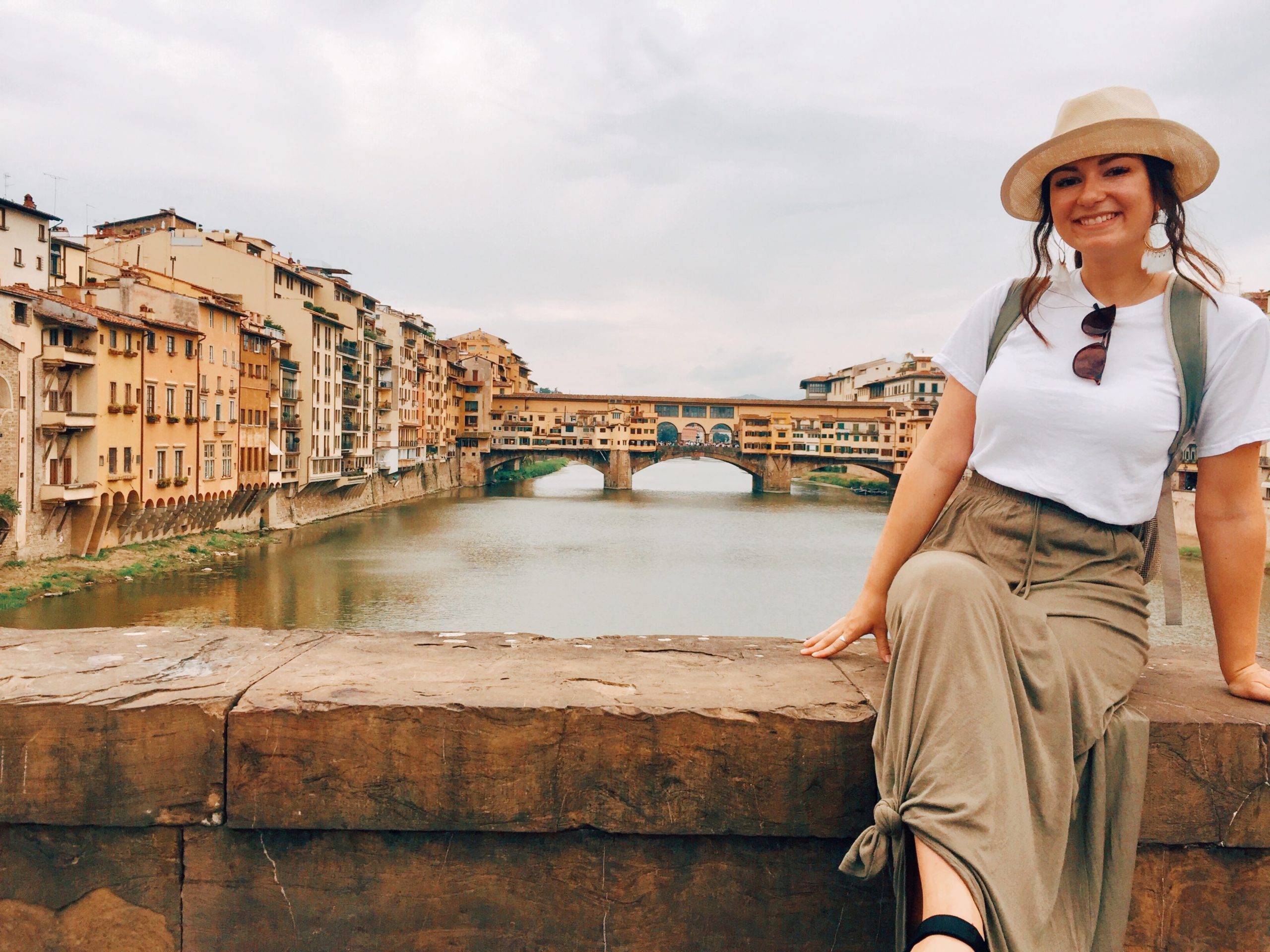 Young woman in straw hat overlooking the Arno River and Ponte Vecchio in Florence, Italy.