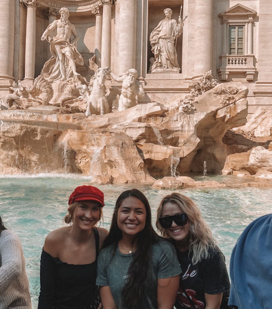 Three young women smiling at Trevi Fountain in Rome, Italy.