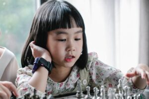 adorable ethnic child doing move while playing chess with grandmother