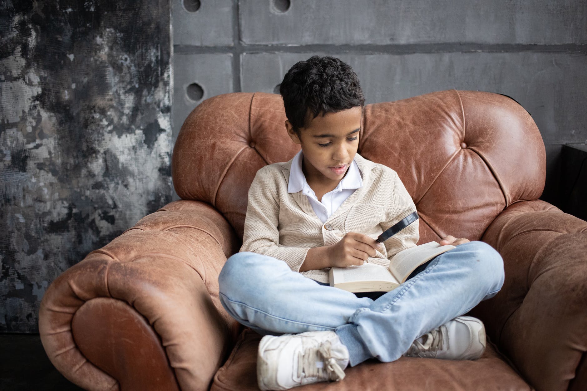 focused arabian schoolboy using magnifying glass to read interesting book