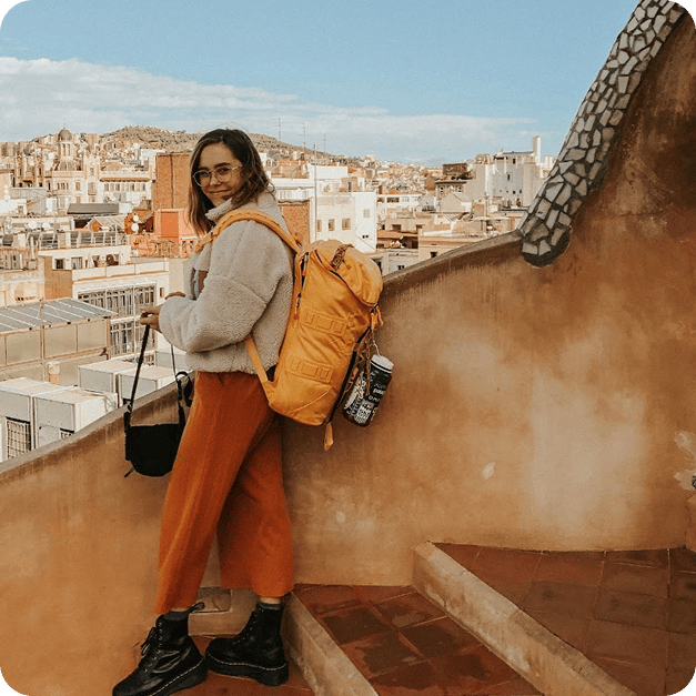 Young woman with yellow backpack overlooking Spanish cityscape from rooftop.