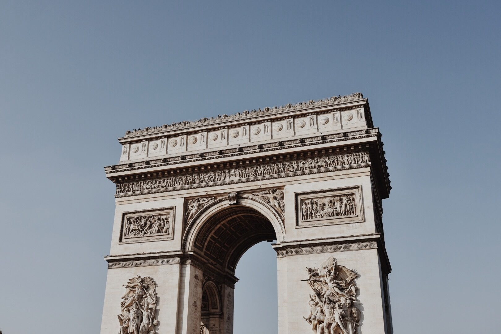 The iconic Arc de Triomphe rises majestically against a clear blue sky in Paris.