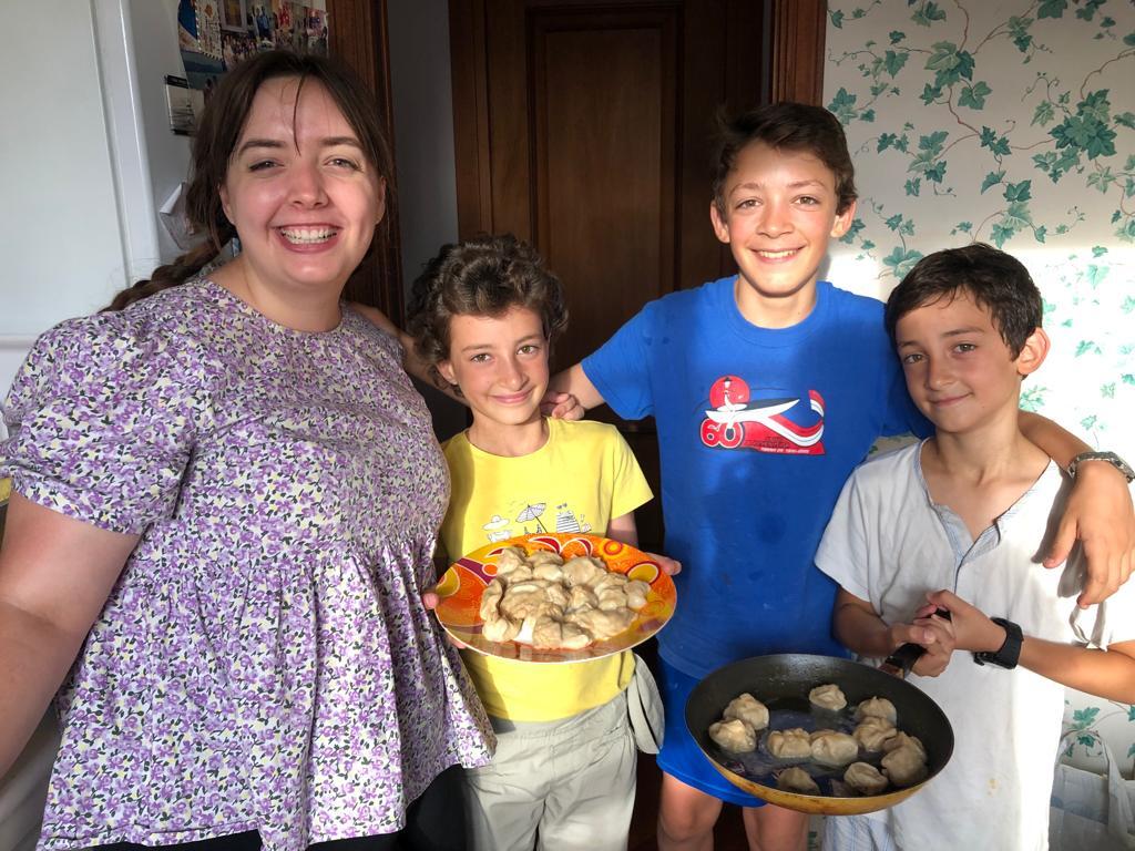 Au pair with three children proudly displaying homemade meal at home.