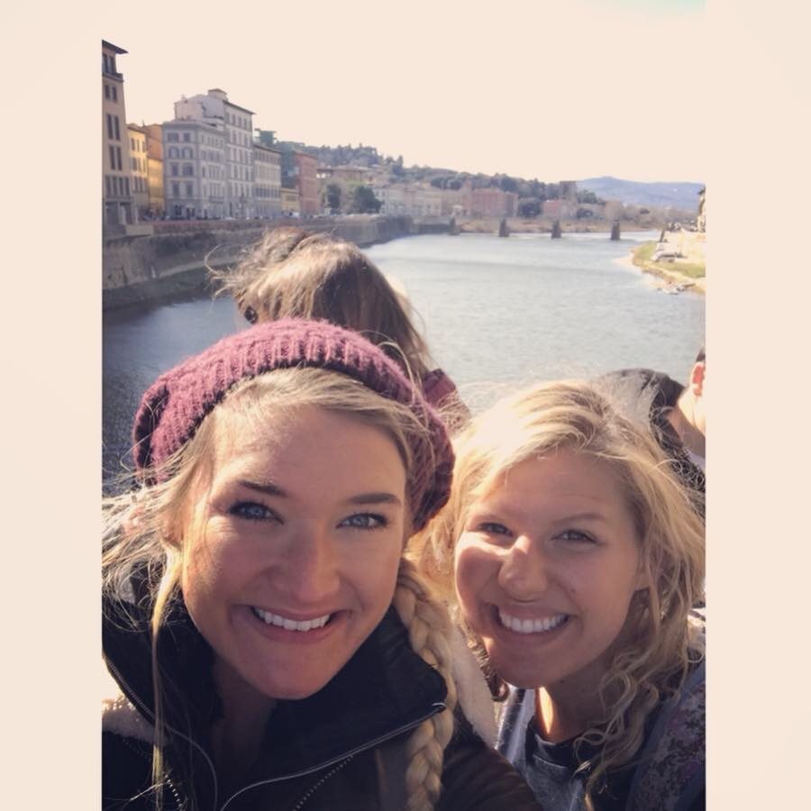 Two young women smiling together by the Arno River in Florence.