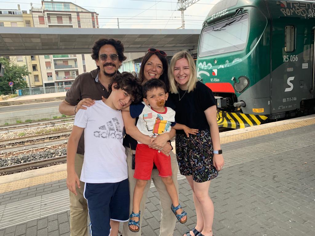 Au pair smiling with her host family on a European train platform.