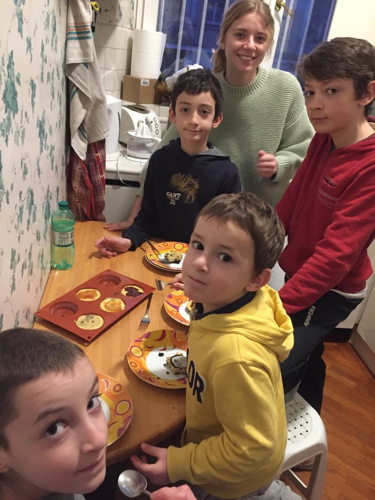 Au pair shares mealtime with children in a cheerful family kitchen setting.