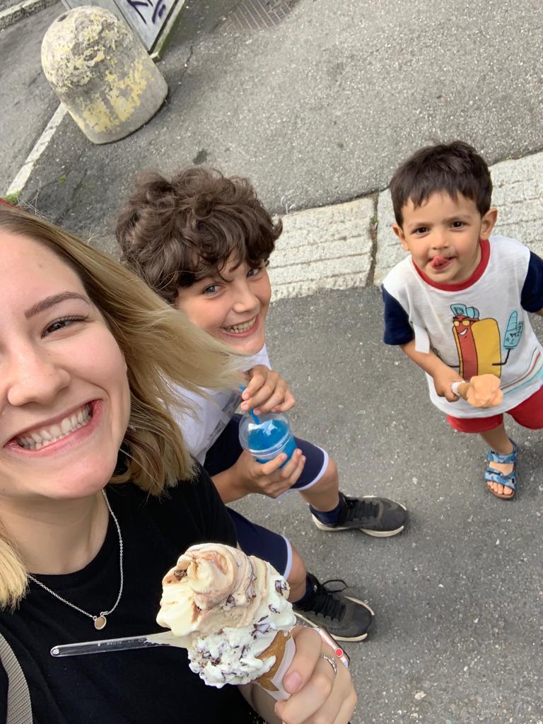 Young caregiver and children sharing gelato on a sunny European street.
