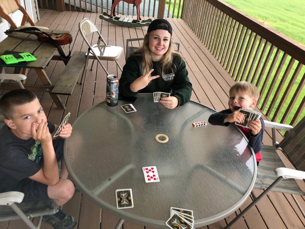 Young woman playing card games with two children on a sunny patio.