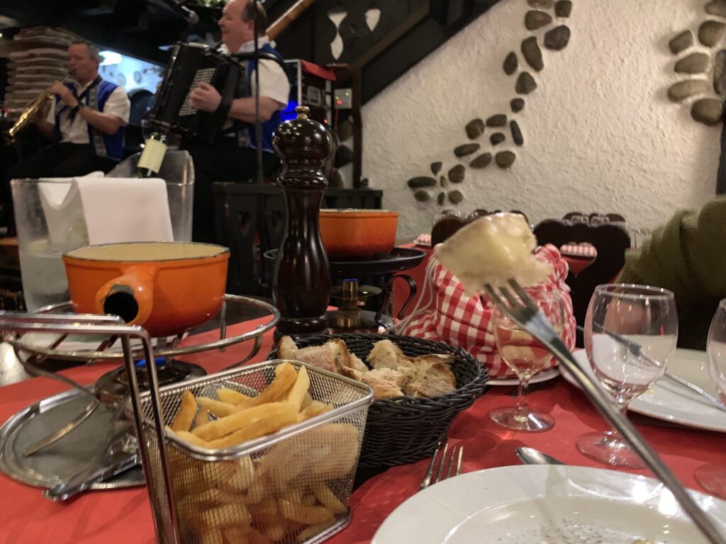 A European dining table spread with fresh bread, fried potatoes, and a traditional fondue pot.