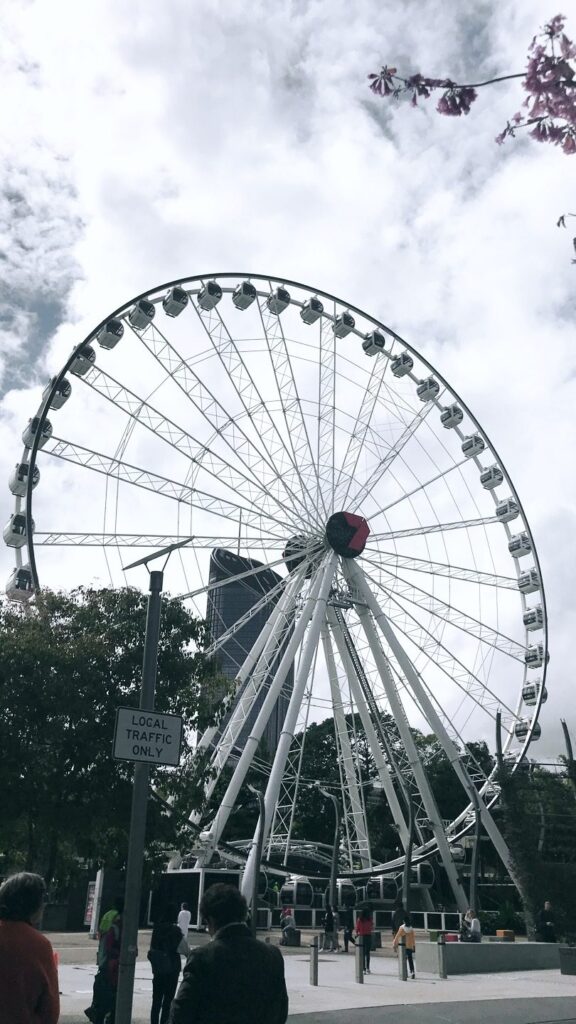 Ferris wheel reaching into a cloudy sky with visitors walking beneath.
