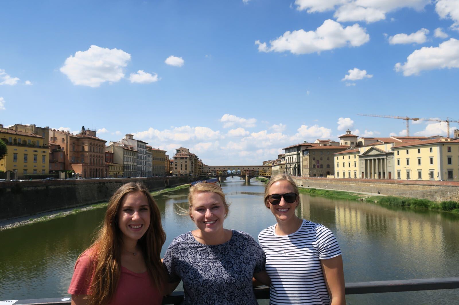 Three young women smile by the Arno River in Florence, Italy.