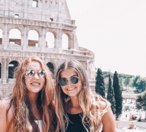 Two friends smile together in front of Rome's Colosseum.