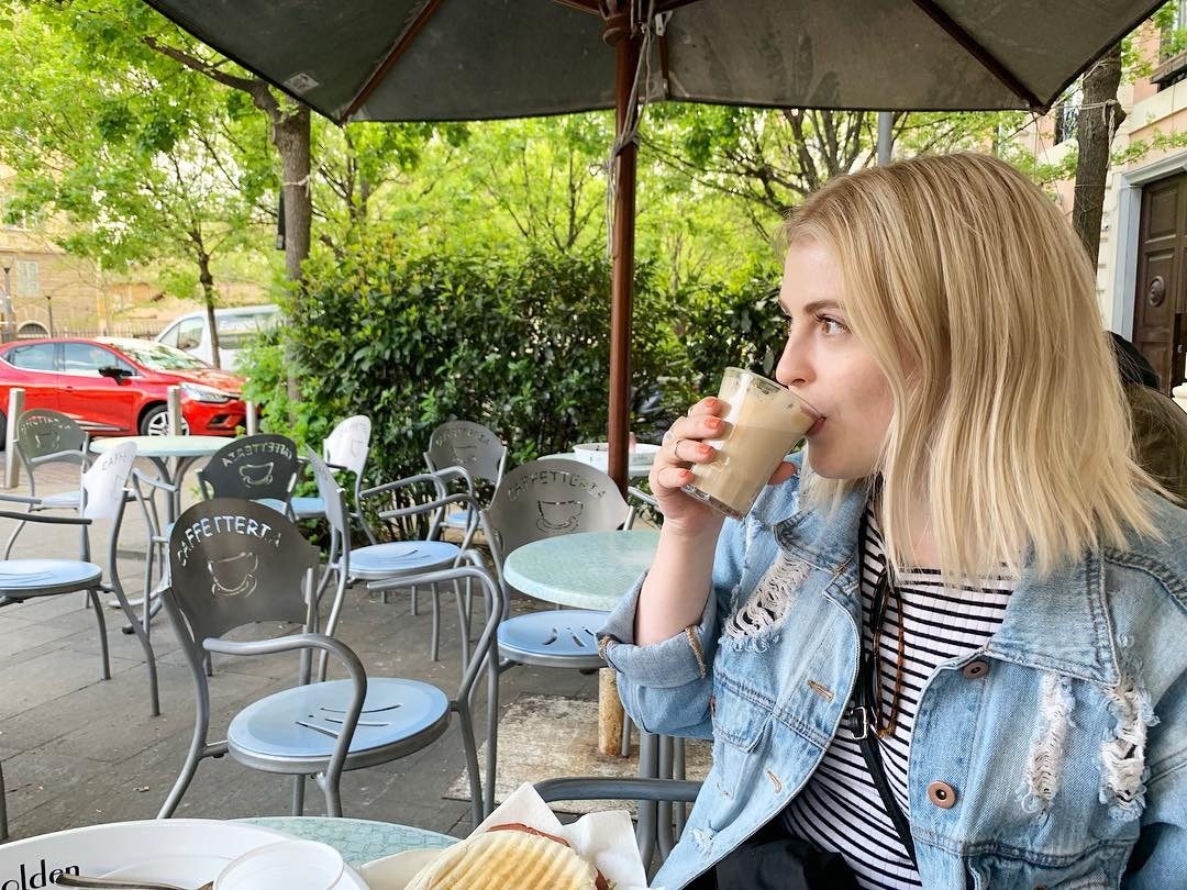 Young woman enjoying an iced drink at a European street café under a green umbrella.