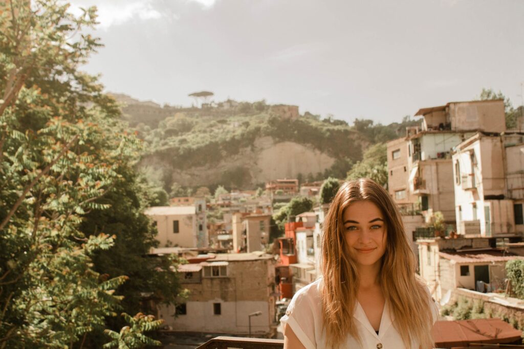 Young woman smiling in front of a Tuscan hillside village with terracotta buildings.